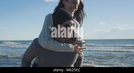 Les hommes Donner Piggy Back Rides au coucher du soleil par la mer, le temps d'automne Banque D'Images