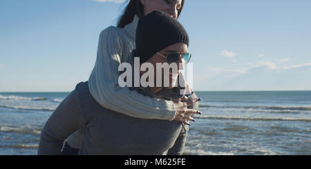 Les hommes Donner Piggy Back Rides au coucher du soleil par la mer, le temps d'automne Banque D'Images