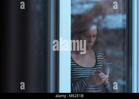 Seul Homme Triste A L Aide De Telephone Mobile Pour Envoyer Des Sms Par La Fenetre En Hiver Apres Midi Alors Qu Il Neige A L Exterieur Teal Et Tons Orange Avec Image Photo Stock Alamy