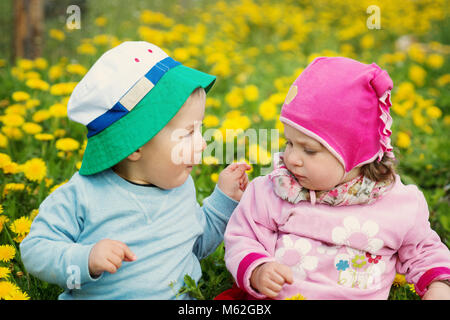 Petit garçon et fille en chapeau assis sur le terrain avec des jouets mous en été Banque D'Images