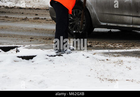 Le travailleur nettoie les voies de chemin de fer de la neige avec une pelle à la place des passages à niveau de l'automobile. Banque D'Images