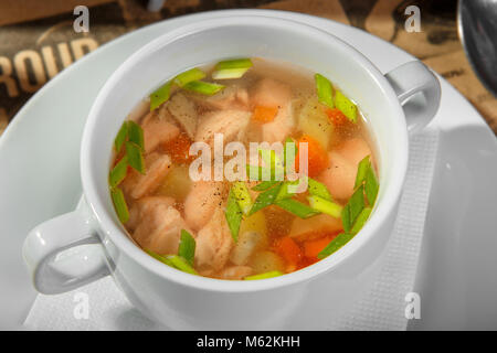 Soupe transparente avec du poulet, du poisson des carottes et des herbes, du poivre noir, dans une assiette blanche. Dépôt d'un restaurant, bar, café. La lumière, faible-calo Banque D'Images