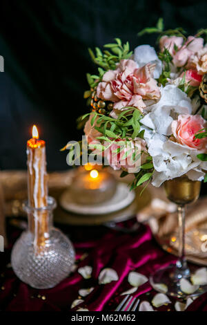 Bouquet dans un vase haut sur l'arrière-plan d'une servi table avec une bougie allumée Banque D'Images