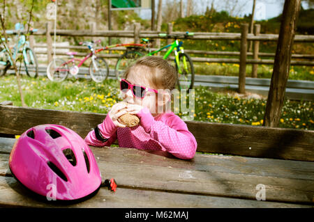 Un blanc bike rider 6 ans, fille d'un déjeuner sur un banc à l'extérieur. Banque D'Images