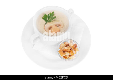 Purée, soupe soupe crème blanc, beige avec des champignons, championons et des craquelins, du pain sec. Sur une serviette dans une assiette blanche blanc isolé. Plats de service i Banque D'Images