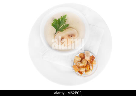 Purée, soupe soupe crème blanc, beige avec des champignons, championons et des craquelins, du pain sec. Sur une serviette dans une assiette blanche blanc isolé. Plats de service i Banque D'Images