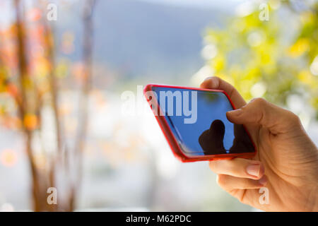 Close up on hand of man using cell phone sur le côté extérieur dès les beaux jours. Smartphone avec couvercle rouge. Accès sans fil à internet concept Banque D'Images