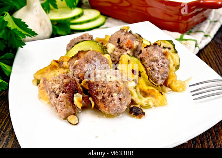 Des boulettes de viande cuite au four avec les courgettes, le fromage et les noix dans une assiette, serviette, ail, persil sur une planche en bois historique Banque D'Images