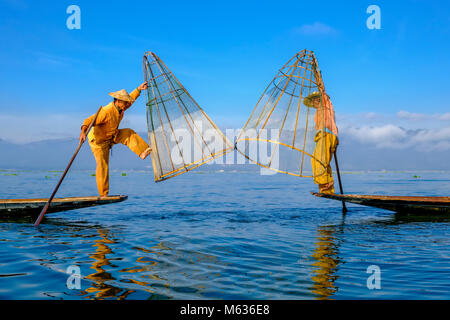 Deux pêcheurs, debout sur leurs bateaux, sont la manière traditionnelle de pêche sur le lac Inle en battant le basketlike filet de pêche dans l'eau Banque D'Images
