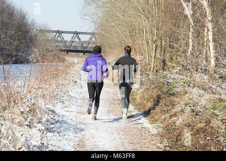 Deux jeunes femmes qui font du jogging le long de la piste de remorquage du canal de Basingstoke dans la neige en ponte, au Royaume-Uni Banque D'Images