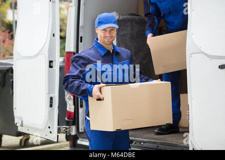 Portrait Of A Smiling Young Delivery Man Carrying Cardboard Box Banque D'Images