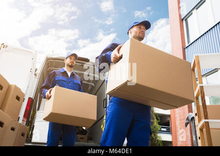 Portrait de deux jeunes hommes livraison Carrying Cardboard Box en avant du chariot Banque D'Images