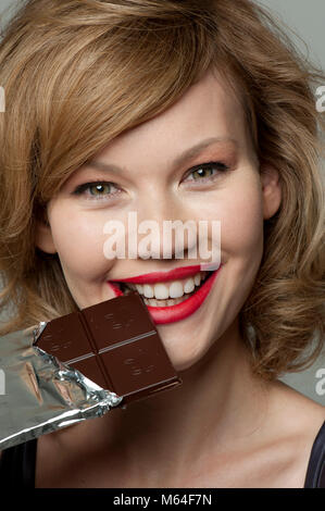 Happy woman biting en bar de chocolat noir Banque D'Images