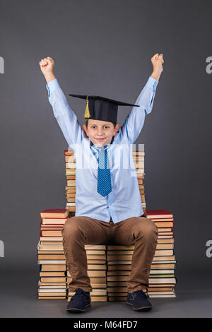 Concept de l'éducation. Happy boy en mortier assis sur un trône, à partir de livres Banque D'Images