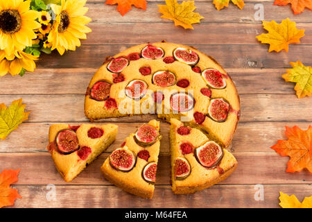 Fig fait maison et gâteau à la framboise avec un bouquet de tournesols et feuilles d'automne sur fond de bois brun foncé. Banque D'Images