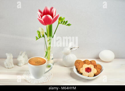 Arrière-plan de café de Pâques. Fleurs de Printemps vase en verre, lapins de Pâques, d'espresso et de cookies en forme de feuilles et de fleurs. Banque D'Images