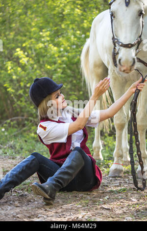 Belle femme assise sur le sol avec cheval brun près de chez elle. Banque D'Images