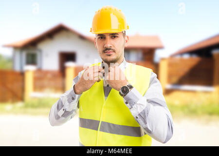 Fier et confiant l'architecte ou le constructeur standing in front of new house fixant son collier comme concept d'emploi fructueuse Banque D'Images