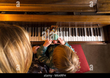 Une jeune mère de race blanche, s'assoit et joue avec son fils devant un piano dans leur salon. Banque D'Images