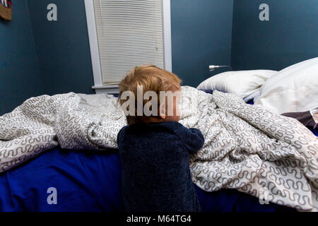 Peu Caucasian Baby Bébé garçon, vêtu de pyjamas, monte dans son lit dans sa chambre Banque D'Images