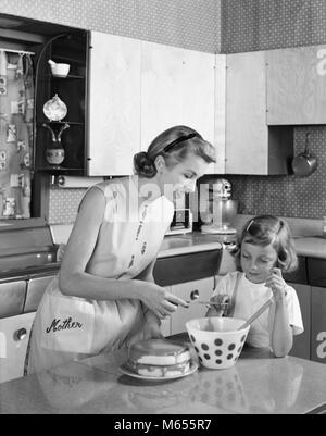 1950 Mère et fille EN GLAÇAGE GÂTEAU CUISINE DOUBLE COUCHE MOT MÈRE SUR TABLIER - asp x16750 CAM001 HARS, filles à l'intérieur des bols nostalgie de givrage AU FOYER ET LES MÈRES AU FOYER DE LA COUCHE DE GIVRE HOUSEWIVES MOT BOL JUVÉNILES B&W NOIR ET BLANC DE L'origine ethnique caucasienne Cuisine île old fashioned personnes montrant de l'enseignement Banque D'Images