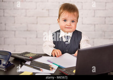 Cute blonde un enfant dans un costume d'affaires est assis au bureau. Courtier infantile avec pour travailler Banque D'Images