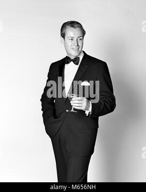 1960 SMILING MAN WEARING TUXEDO HOLDING CHAMPAGNE GLASS - f12257 HAR001 HARS, UNE PERSONNE SEULE COPIE DE LUXE demi-longueur à l'intérieur de l'espace NOSTALGIE CONFIANCE 30-35 ans 35-40 ans succès TUX BONHEUR JOYEUX LOISIRS RELAXATION STYLES BOISSONS loisirs sophistiqués beau sourire de fierté JOYEUSE FASHIONS ATOURS ATTRAYANTS Calme Confiant les mâles adultes mi-MID-ADULT MAN B&W BLACK AND WHITE BLACK TIE de l'origine ethnique caucasienne recueillis à l'ANCIENNE DÉBONNAIRE PERSONNES COURTOIS Banque D'Images