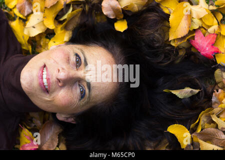 Portrait de femme mature charmante sentiment confortable étendue sur le sol plein de jaunes et bruns feuilles dans le parc en saison d'automne. Concept visionnaire Banque D'Images
