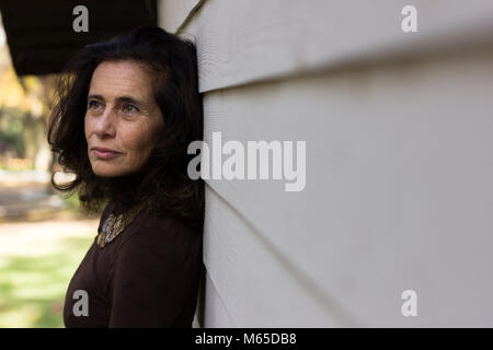 Femme mature sérieux sur pull marron collier et appuyé contre le mur blanc planche en bois. Concernées, regard inquiet concept Banque D'Images