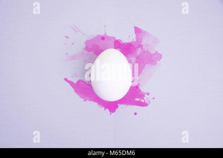 L'un des oeufs blancs sur fond lilas pastel aquarelle rose avec des éclaboussures. Banque D'Images