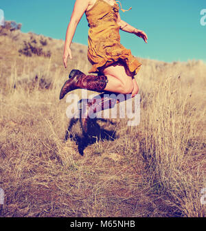 Jolie femme dans une jupe sauter de haut en bottes de cow-boy dans un champ de blé sur une chaude journée d'été tachée vintage retro filtre instagram Banque D'Images