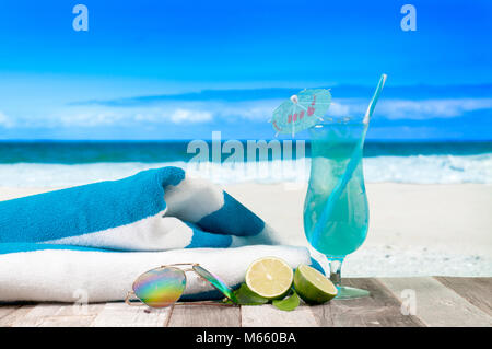 Vacances d'été sur le bord de la mer. Verre de cocktail, une serviette et des lunettes de soleil sur la plage. Banque D'Images