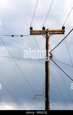 En bois ancien pilier électrique avec des connexions et des lignes de transport d'aller dans toutes les directions contre ciel orageux Banque D'Images