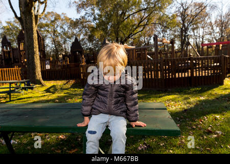 Un enfant de race blanche se repose sur une table de pique-nique vert à un parc public Banque D'Images