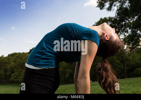 Young Caucasian Woman pratique le yoga dans Central Park NYC EN PORTANT UN HAUT Bleu, guêtres noires et Barefoot Banque D'Images