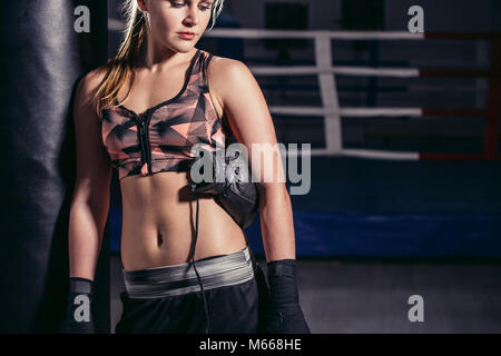 Boxer femme se pencher en avant pour se reposer sur un énorme sac de frappe Banque D'Images