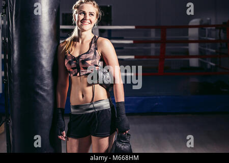 Boxer femme se pencher en avant pour se reposer sur un énorme sac de frappe Banque D'Images
