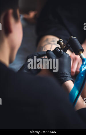 Artiste masculin de tatouage fait un tatouage sur la jambe d'une femme. Banque D'Images