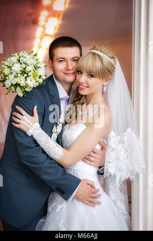 Le marié et la mariée avec un bouquet de mariage se tiennent près de la colonne blanche Banque D'Images