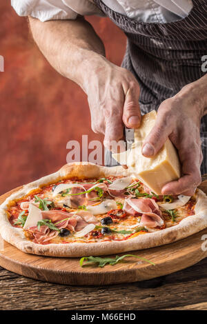 Pizza et Chef. Le chef du restaurant prépare une pizza et décore avec du parmesan. Banque D'Images