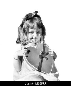 1930 SMILING GIRL HOLDING JUVÉNILE HEART SHAPED CANDY BOX LOOKING AT CAMERA - v157 HAR001 AMITIÉ HARS VALENTINES mi-longueur à l'intérieur FORME SAINT NOSTALGIE CONTACT OCULAIRE 7-9 ans 5-6 ans l'EXCITATION JOYEUSE SAINT VALENTIN LE BONHEUR JOYEUX SOURIRES ST. Les juvéniles SYMBOLIQUE VALENTINES DAY B&W NOIR ET BLANC DE L'ORIGINE ETHNIQUE CAUCASIENNE BONBONS FÊTE LE 14 FÉVRIER EN FORME DE CŒUR À LA CAMÉRA À ST à l'ANCIENNE. VALENTINE Banque D'Images