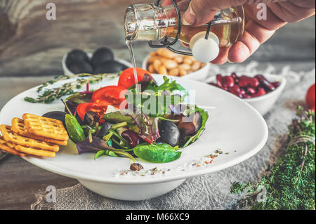 Verser la salade huile d'olive régime pour la correction du poids des feuilles de Lollo Rosso, Cresson et autres herbes verte, tomates, olives et fitaki. Banque D'Images