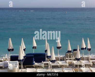 Parasols fermés bleu et blanc et vide de chaises longues sur une plage de galets Banque D'Images