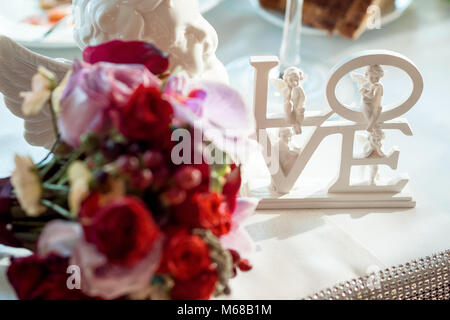 Vue rapprochée de la lettres blanches ''love'' décoré avec des anges placés sur la table près de bouquet de roses colorées floues. Banque D'Images