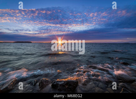 Coucher du soleil sur une plage de rochers avec des vagues se précipiter dans Banque D'Images