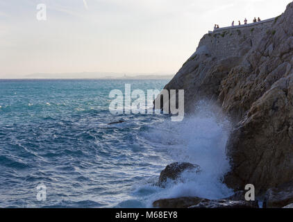 Côte Rocheuse à Nice, en France, avec les vagues qui les rochers et certaines personnes sur la promenade sur le haut de la falaise Banque D'Images