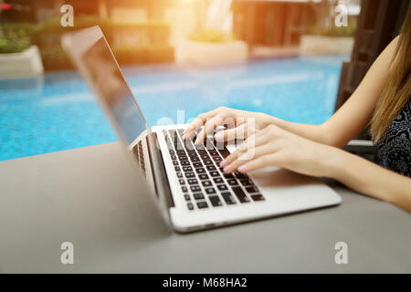 Close up femme mains appuyant sur le clavier sur pc portable journée ensoleillée piscine Banque D'Images