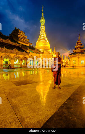 Un moine bouddhiste est debout devant la pagode Shwemokhtaw d'or, est le plus grand temple de la ville, la nuit Banque D'Images