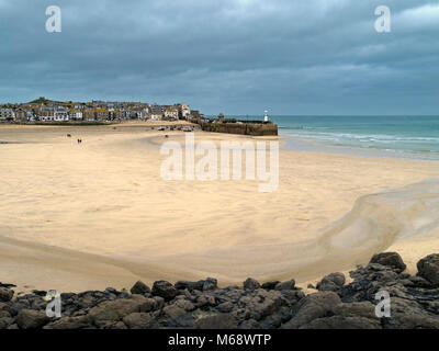 Grande plage de sable à marée basse avec le port et la ville côtière de St Ives au loin avec un ciel gris foncé, Cornwall, England, UK Banque D'Images