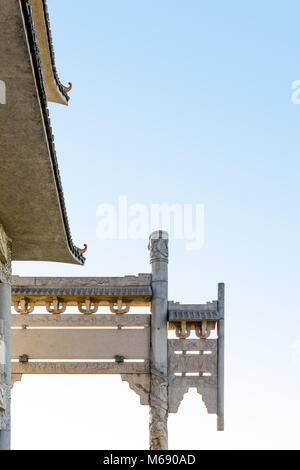 Porte traditionnelle chinoise faite de béton et de toits courbés d'une pagode contre un ciel bleu. Banque D'Images